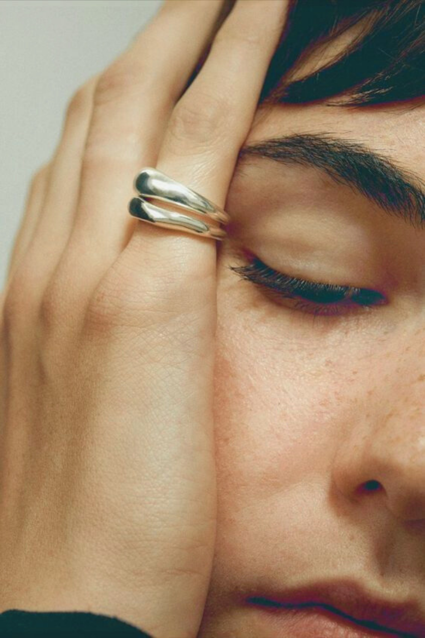 Close-up of a hand with stacked silver rings resting on a face